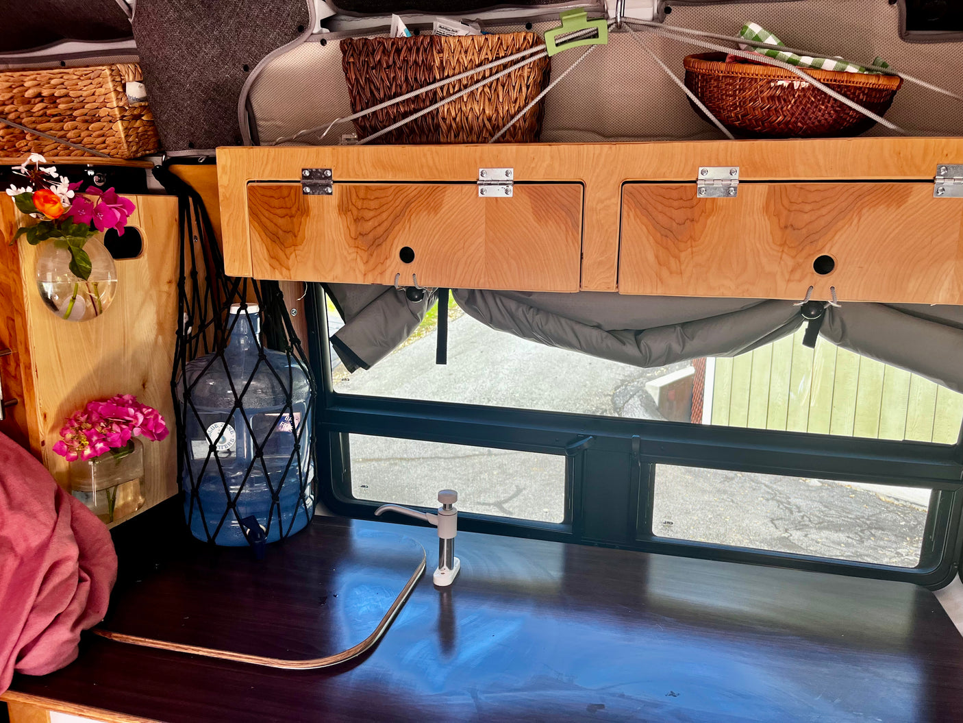 Inside an RV rental: a practical kitchenette with pump, built-in storage, and bright window views. Perfect for travel.