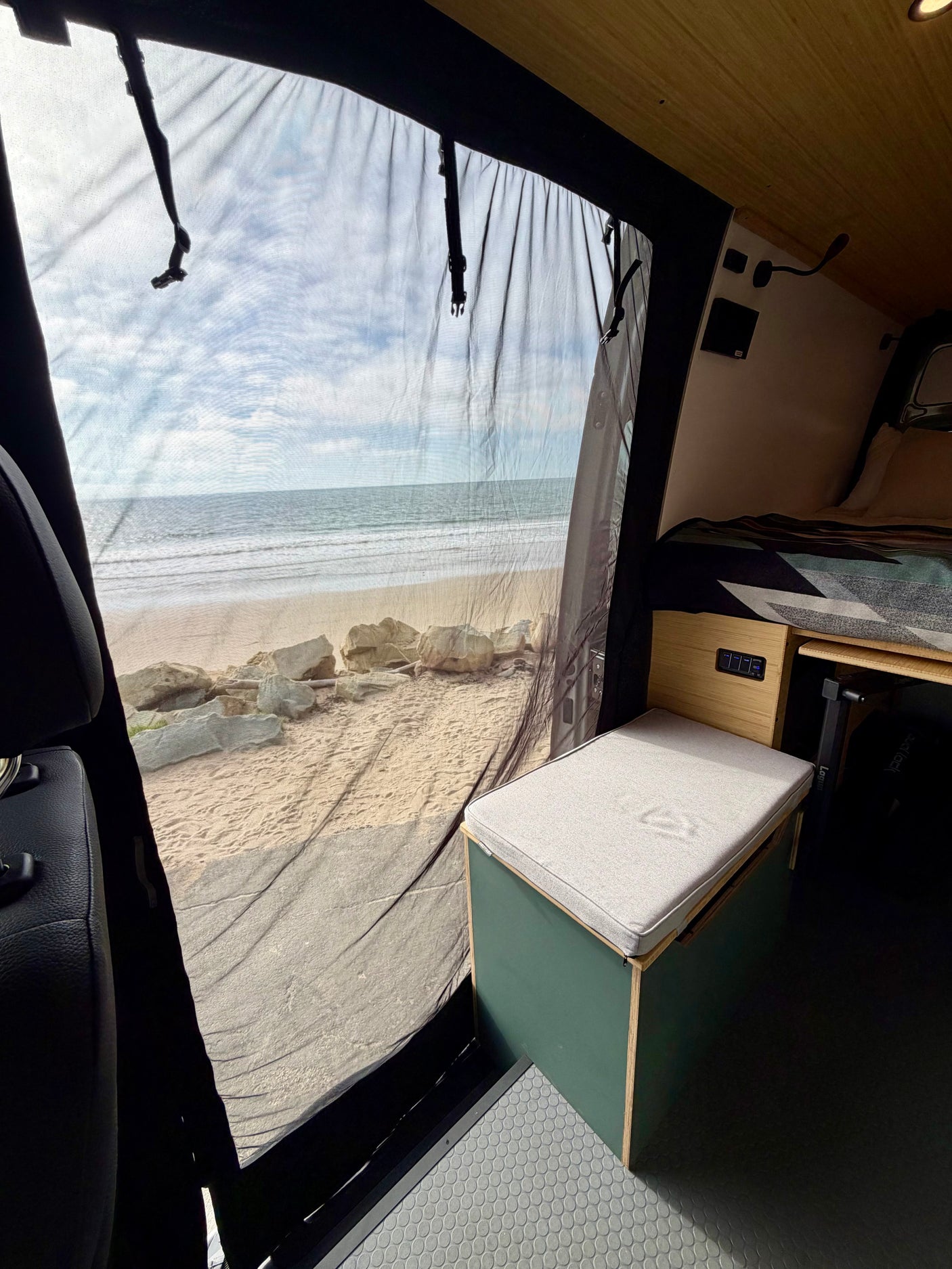 Experience oceanfront travel in this rv rental! A comfortable seat & bed inside a van with a stunning beach view through a mesh screen.