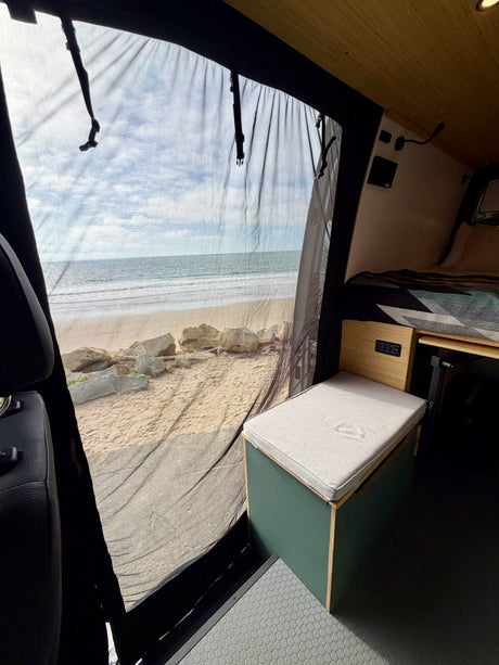Experience oceanfront travel in this rv rental! A comfortable seat & bed inside a van with a stunning beach view through a mesh screen.