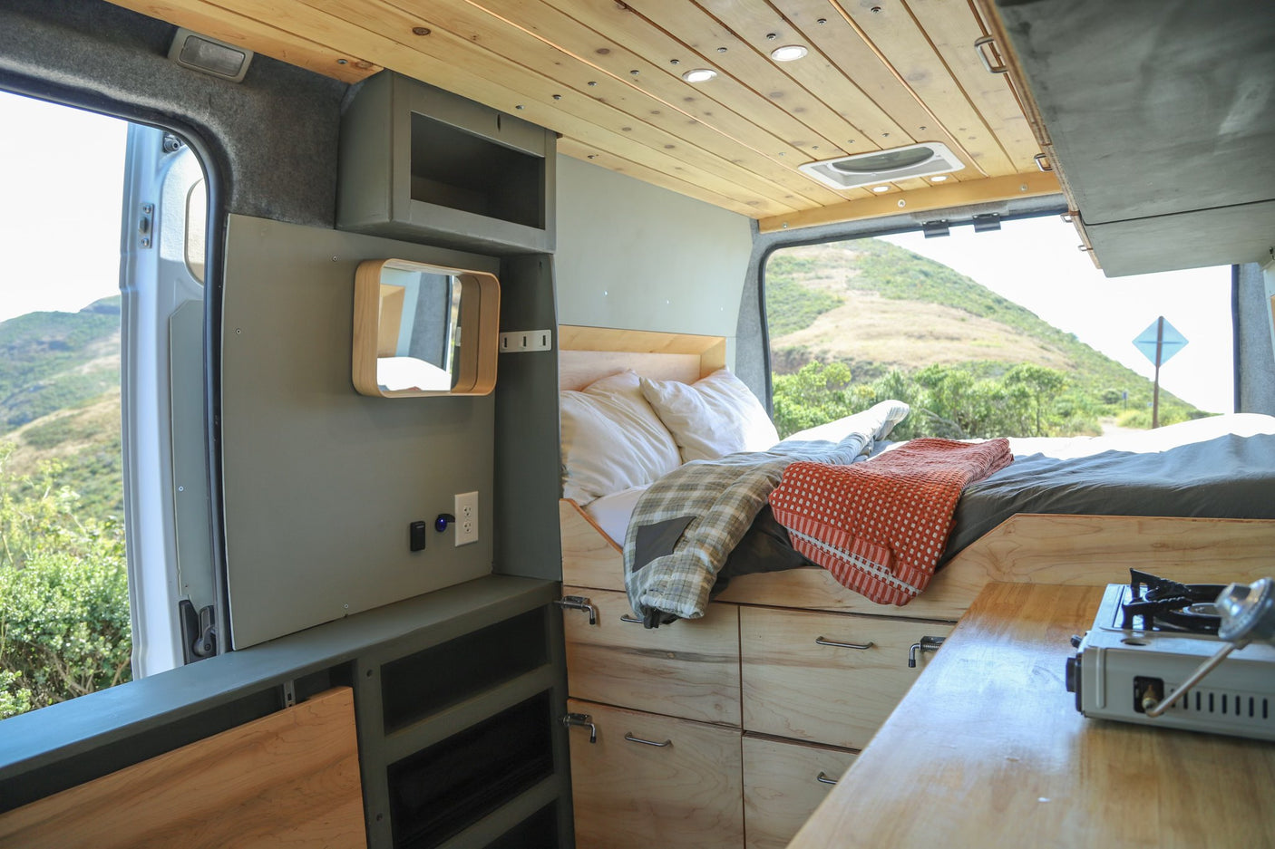 Experience van life! This RV rental features a cozy bed, kitchen space with stove, & scenic views out the open doors.