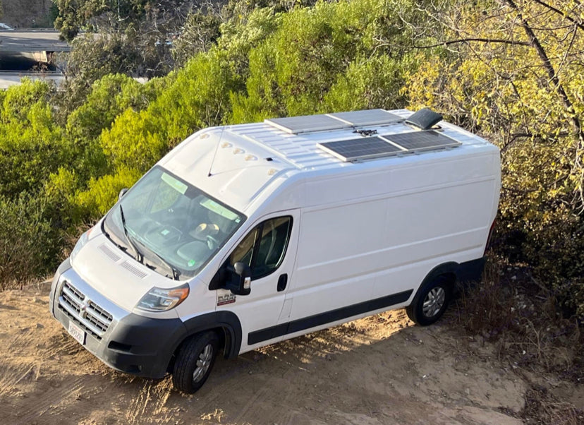 White RV rental camper van with solar panels on roof, parked on a dirt path. Perfect for off-grid van life adventures.