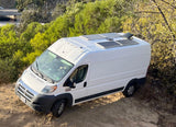 White RV rental camper van with solar panels on roof, parked on a dirt path. Perfect for off-grid van life adventures.