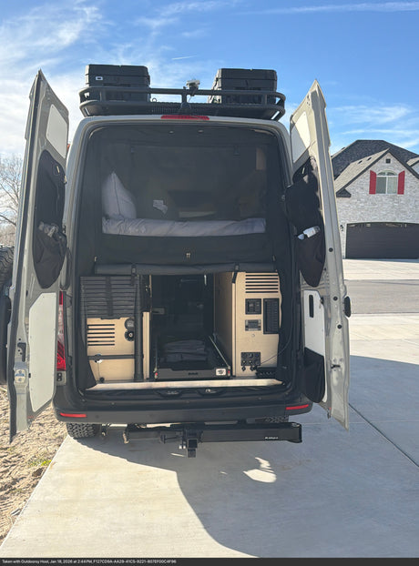 This RV rental camper van, with open rear doors, showcases a customized interior, sleeping area, storage, and roof rack.