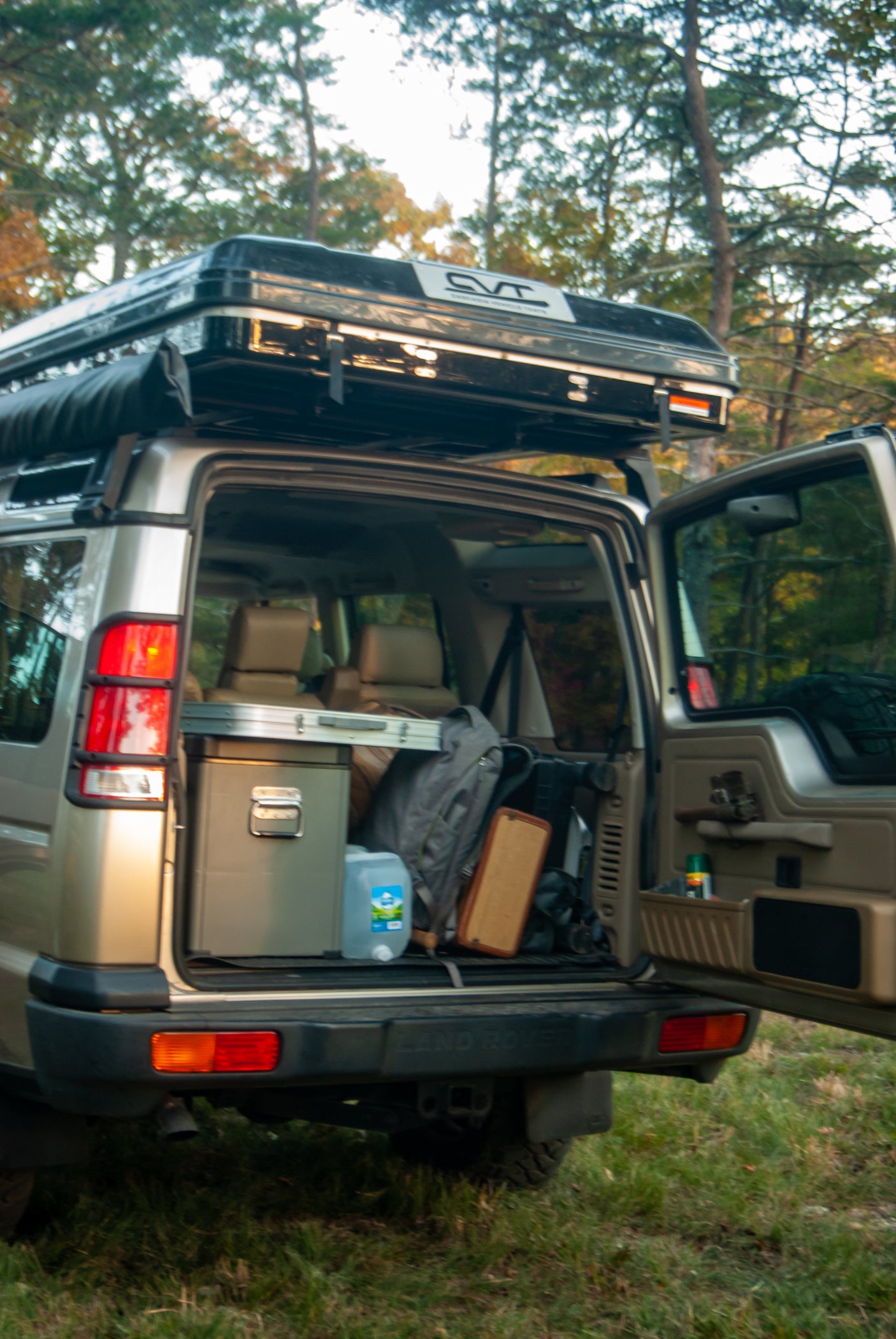 RV rental-ready Land Rover Discovery SUV: open trunk reveals cooler & gear, with a rooftop tent on top. Ideal for overlanding.