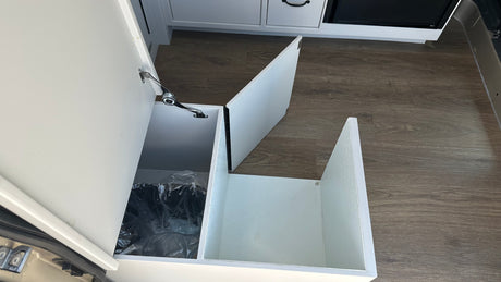 RV rental interior with a clever, pull-out trash bin and additional storage space in white cabinetry, ideal for travel.