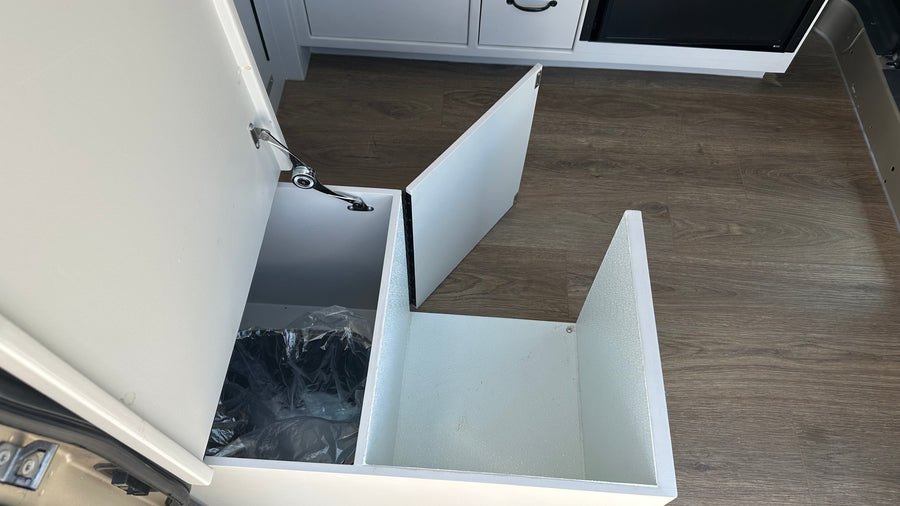 RV rental interior with a clever, pull-out trash bin and additional storage space in white cabinetry, ideal for travel.