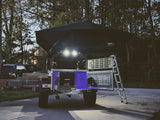 Off-road RV rental: a camping trailer with rooftop tent, ladder, and illuminated power/storage setup.