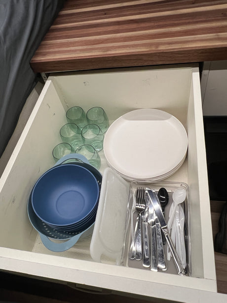 RV rental kitchen drawer stocked with plates, glasses, blue bowls, and cutlery, neatly organized for meals on the road.