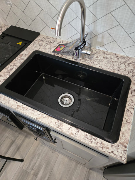 Sleek RV rental kitchen featuring a black sink, brushed stainless faucet, speckled counter, and herringbone backsplash. Stove visible.