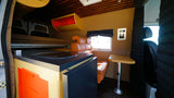 Experience comfort in this RV rental's interior: modern kitchenette, raised bed, and bright living space with seating.