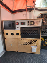 RV rental interior: custom power/control panel with monitor, outlets, HVAC vents, and integrated crate storage for camper convenience.