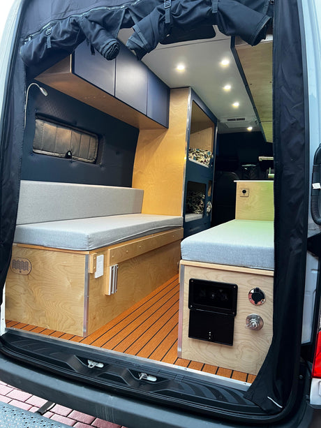 This inviting RV rental's camper van interior features light wood, grey cushions, bunk beds, and a slatted floor, seen from the rear.