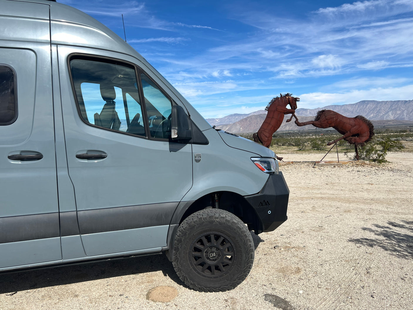 Explore with our rv rental adventure van! Parked in desert by metal horse sculptures & mountains under a blue sky.