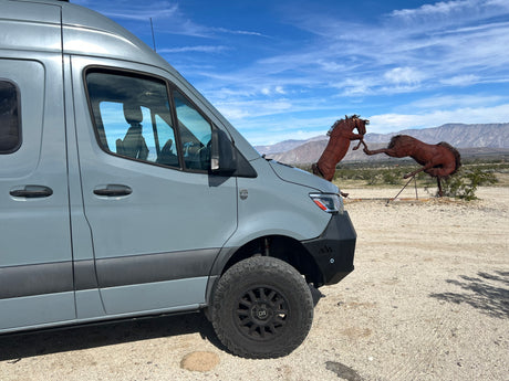 Explore with our rv rental adventure van! Parked in desert by metal horse sculptures & mountains under a blue sky.