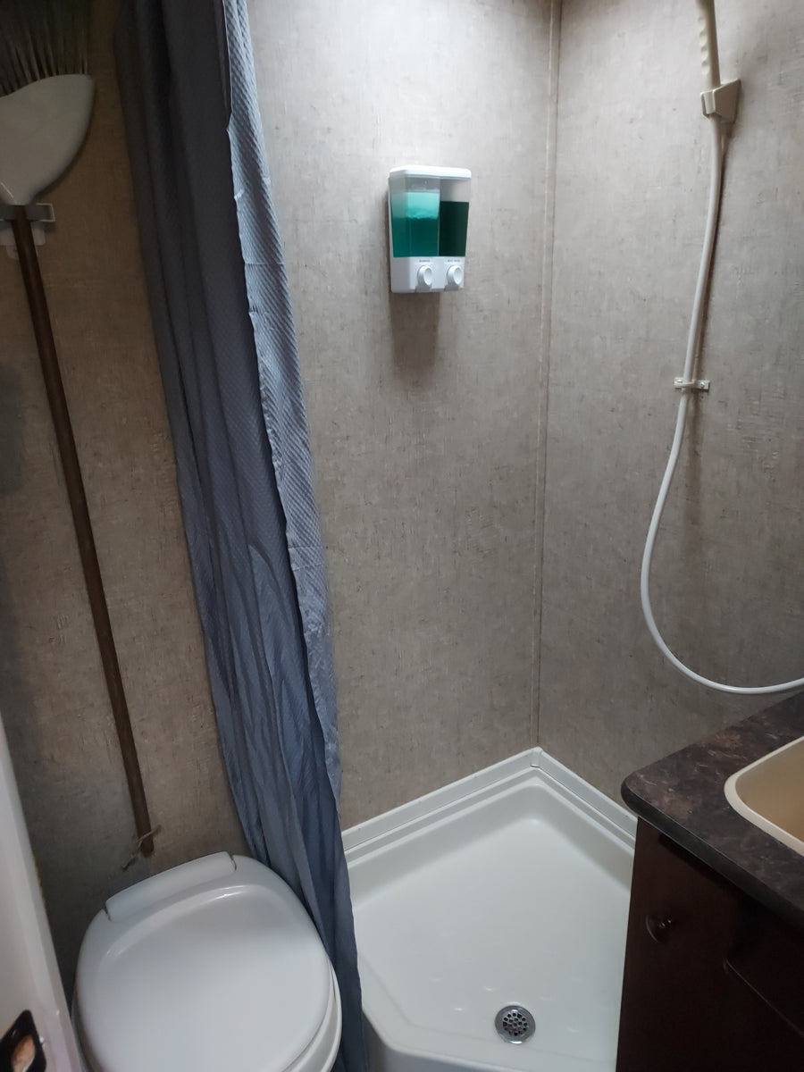 Overhead view of an RV rental bathroom with a white shower base, toilet, sink area, and wall-mounted soap dispenser.