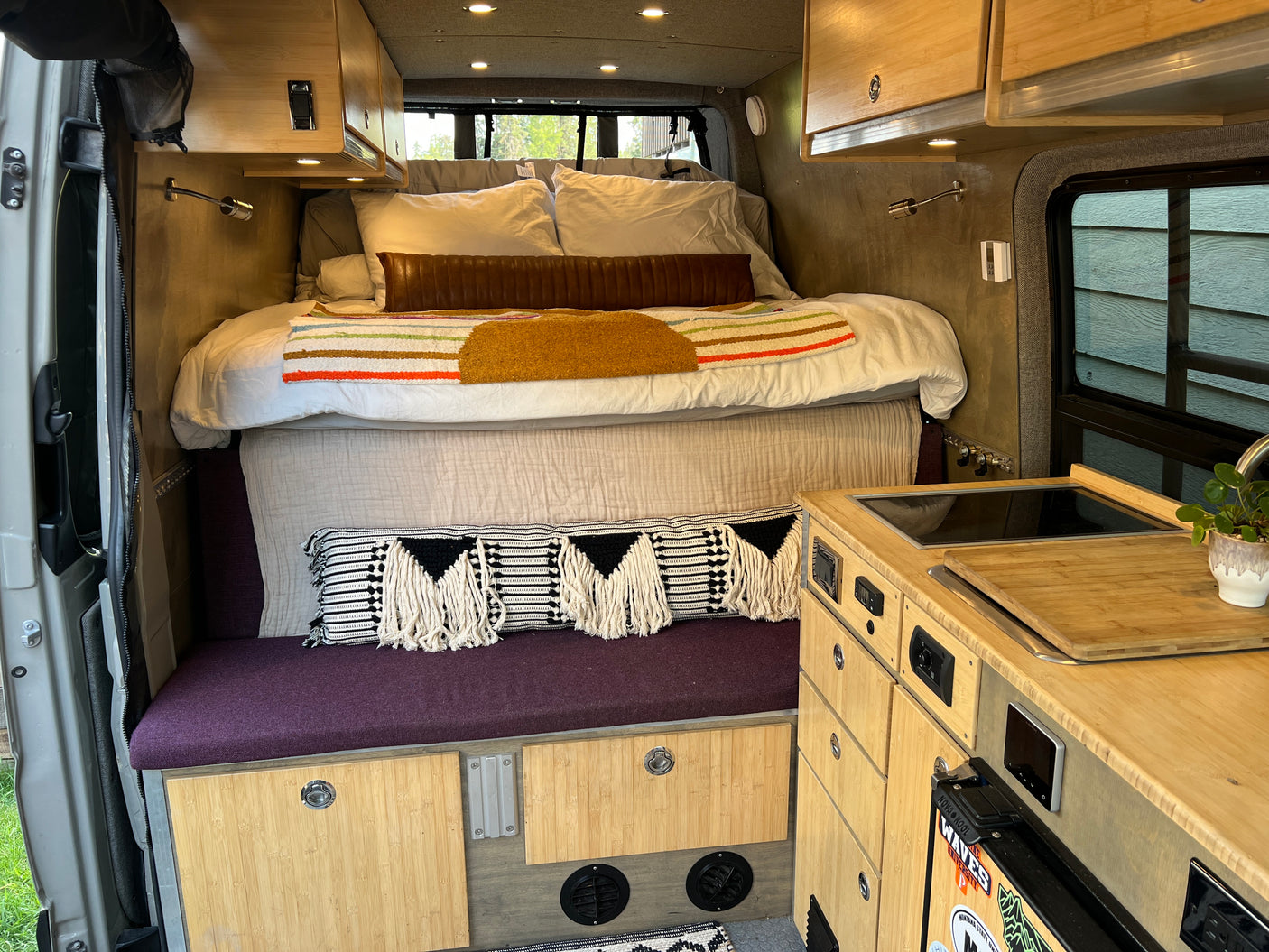 Inside an RV rental: a compact bed, kitchenette, and bamboo cabinetry for nomadic adventures.