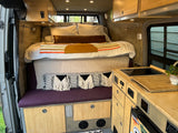 Inside an RV rental: a compact bed, kitchenette, and bamboo cabinetry for nomadic adventures.