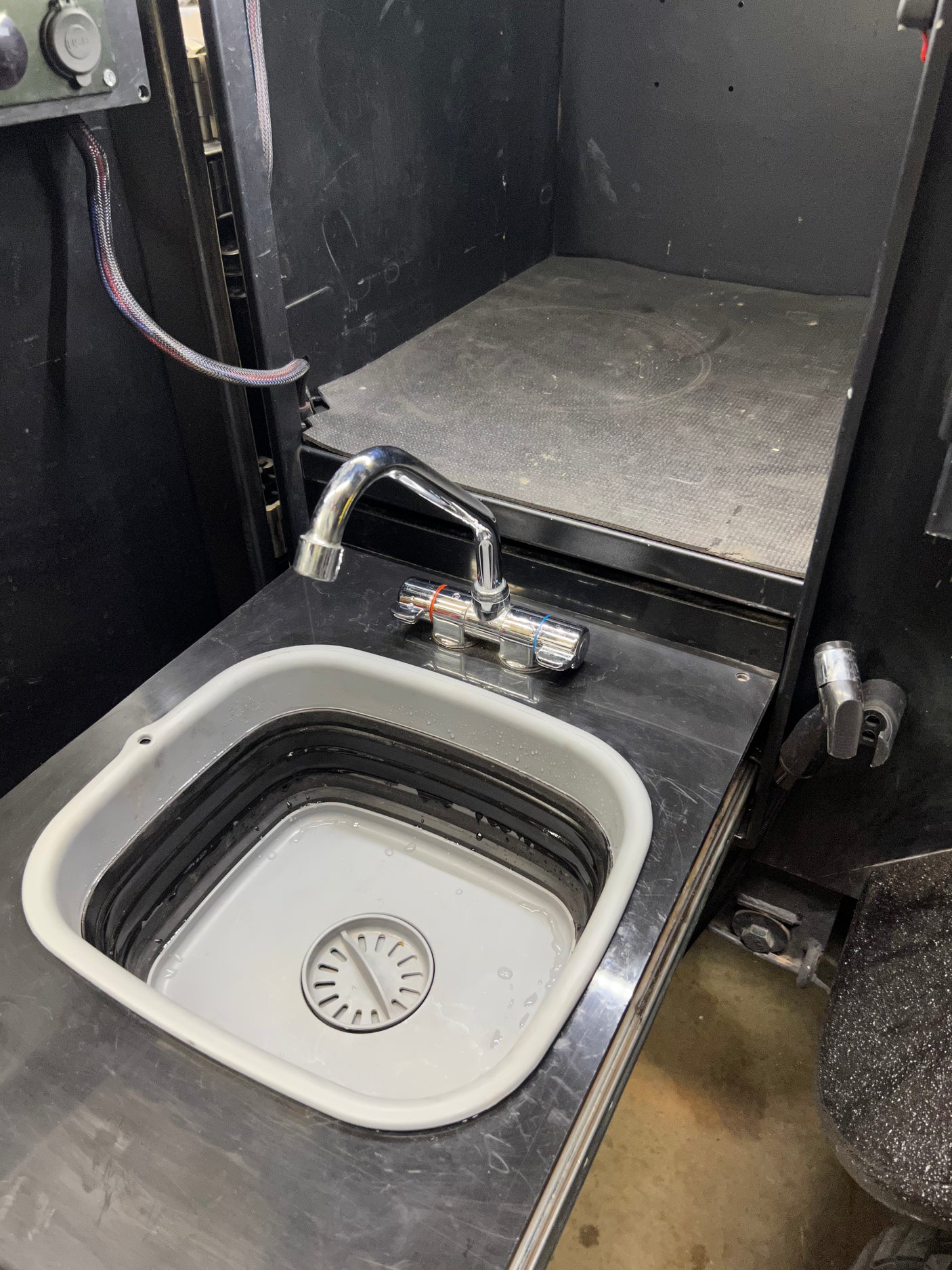 RV rental utility space: a chrome faucet above a collapsible sink, set into a black countertop, with a power outlet panel nearby.