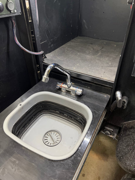 RV rental utility space: a chrome faucet above a collapsible sink, set into a black countertop, with a power outlet panel nearby.
