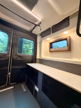 This RV rental's custom interior features bright overhead lighting, mesh storage, a built-in counter, and ample windows for scenic views.