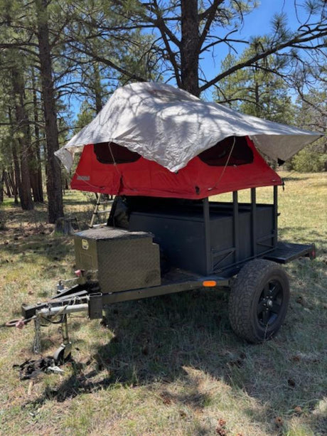 This camping trailer with a red rooftop tent & tarp is an excellent RV rental option for forest adventures.