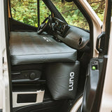 Inside an RV rental, a Luno inflatable mattress spans the front seats, creating a cozy bed with footwell support for camping comfort.