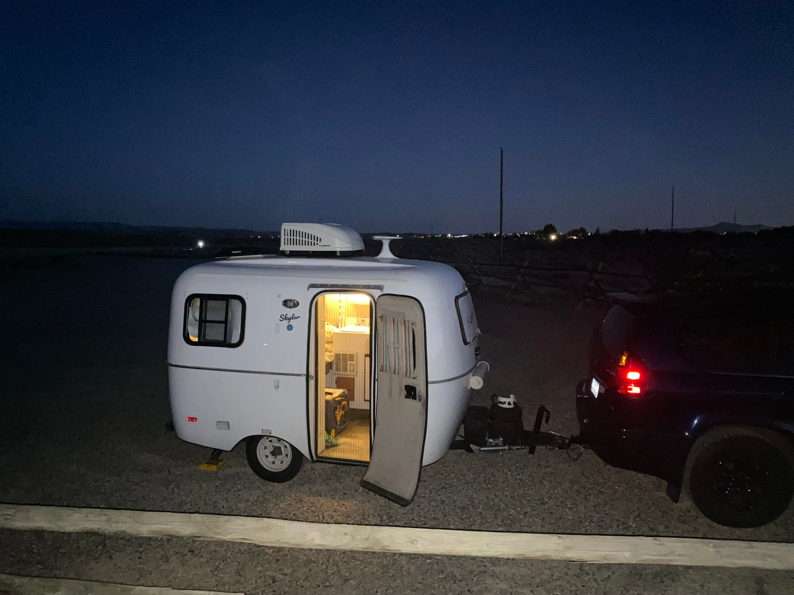 Compact RV rental at night, showing its illuminated interior and an attached SUV, ready for a cozy outdoor adventure.