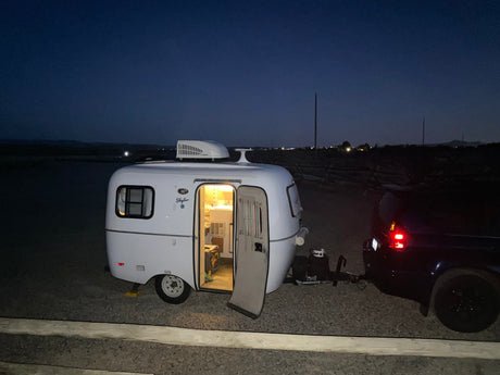 Compact RV rental at night, showing its illuminated interior and an attached SUV, ready for a cozy outdoor adventure.