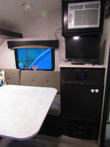 Inside this RV rental: a dinette with table & benches, window, AC unit, TV, stereo, & mini-fridge. Equipped for comfort.