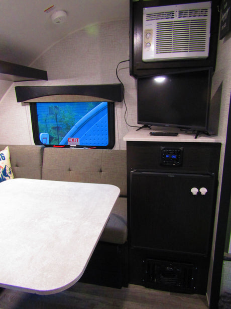 Inside this RV rental: a dinette with table & benches, window, AC unit, TV, stereo, & mini-fridge. Equipped for comfort.