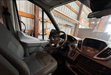 RV rental: View of a spacious van interior from the driver's side, showing dashboard and seats. Parked in a workshop.