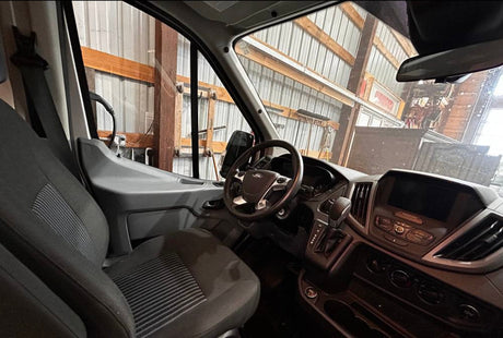 RV rental: View of a spacious van interior from the driver's side, showing dashboard and seats. Parked in a workshop.