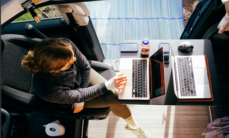 Woman creates a mobile office setup in her RV rental, working comfortably on her laptop with multiple devices on a table.