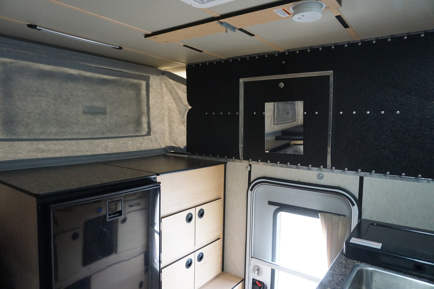 Inside this RV rental: compact kitchen with fridge, wood storage, and view of the pop-top canvas wall. Mobile living. — photo 6