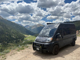 Dark gray RV rental van on a dirt mountain overlook, offering stunning views of a winding river and forested valley below.