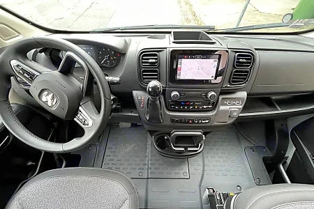 View of an RV rental van's modern cockpit, featuring the driver's steering wheel, dashboard, and navigation screen.