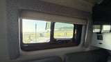 From an RV rental, a sunny window view of a coastal path with people, ocean, and green landscape. Patterned trim & USB port visible.