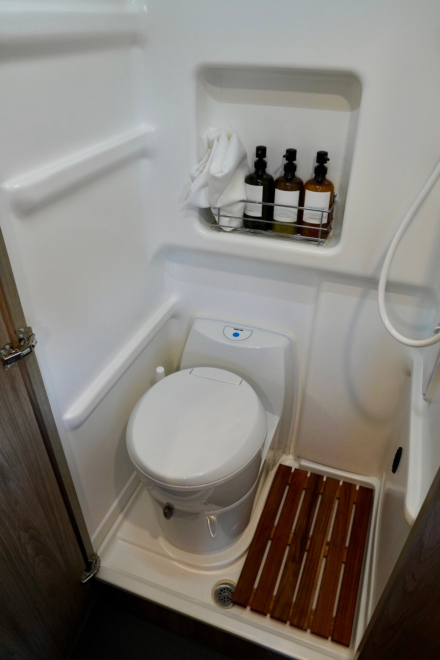 This RV rental bathroom offers a compact design with toilet, shower, wooden mat, and toiletries for comfortable travel.