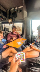 Inside a cozy RV rental, a family laughs while playing cards, making the most of a rainy travel day.