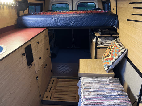 RV rental: Inside a custom camper van with an elevated bed, kitchen counter, and clever storage solutions.