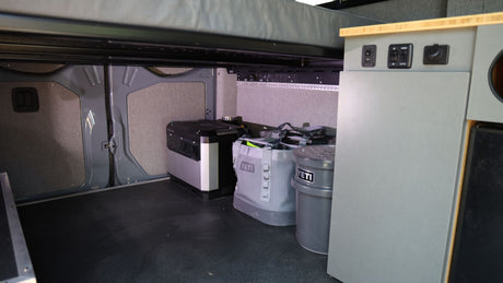 RV rental van interior features organized mobile living storage: portable power station, Yeti cooler, and cabinet controls.