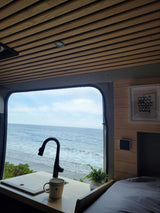 Scenic RV rental interior with ocean view, kitchenette, and bed. Perfect for a cozy beach getaway.