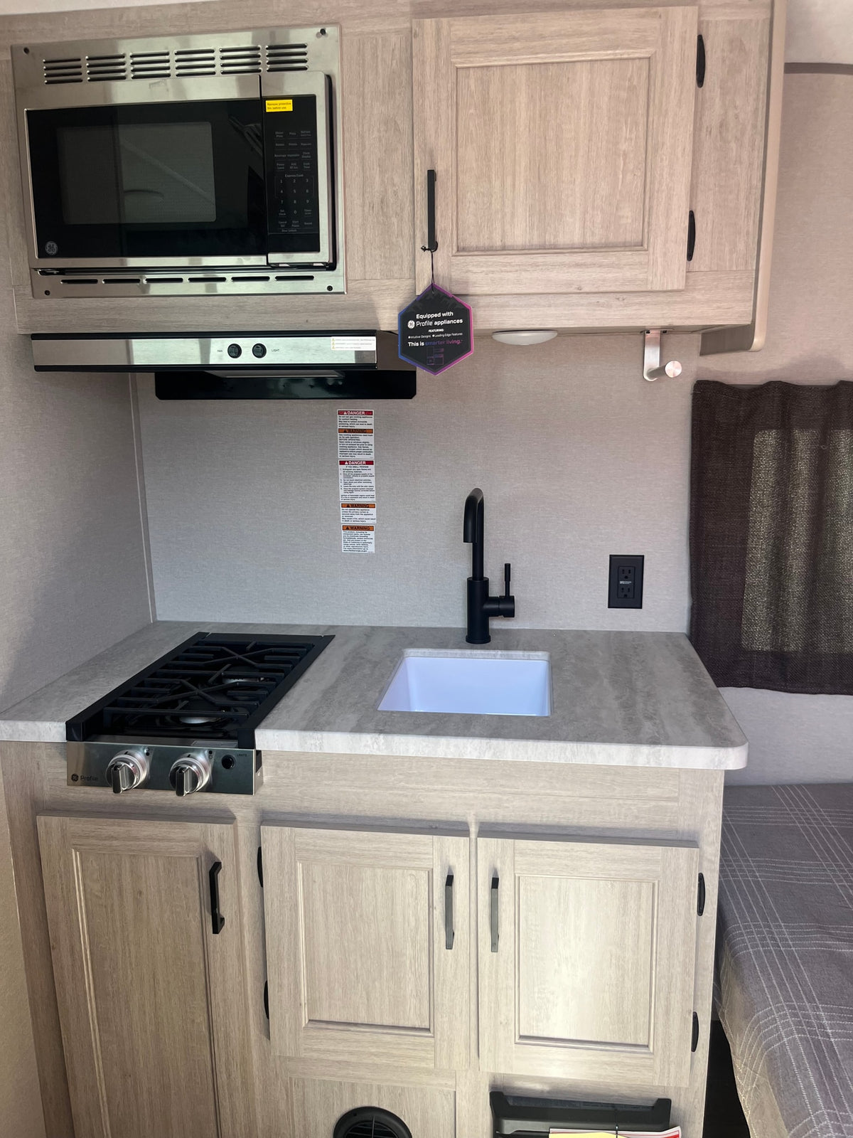 Modern rv rental kitchen featuring a GE Profile microwave, compact gas stove, and sink, designed for efficient travel living. — photo 4