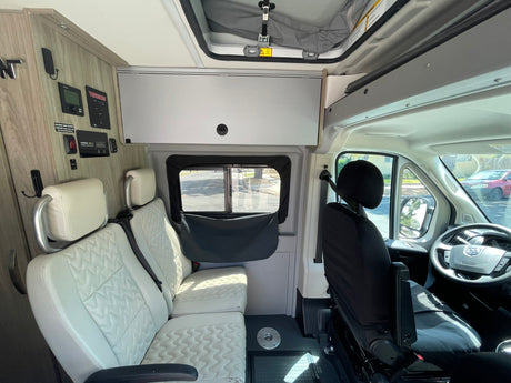 RV rental interior: View of modern camper van's controls, light quilted seats, and front cab area.