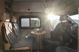 Experience RV rental comfort: interior with dining table, cups, bowl, and two seats. Scenic mountain view with sun glare.