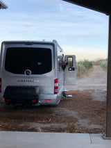 Adventure awaits! A smiling woman peeks from a sleek silver Airstream rv rental parked on a rustic path, ready for a road trip.
