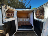 Inside this customized RV rental, an open view reveals a cozy wood-paneled interior with built-in cabinets and turtle window covers.
