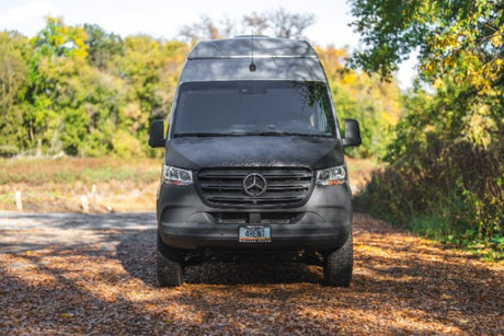 A dark grey Mercedes-Benz Sprinter camper van, marked '4RENT', on a leaf-covered path. Ideal for your next RV rental adventure.