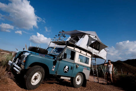 Experience remote adventure with this unique 4x4 overland RV rental & rooftop tent. Person stands by the deployed camp.