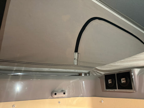 RV rental interior: pop-top fabric, dual USB ports, and a coiled hose (likely for light or shower) provide camper comfort.